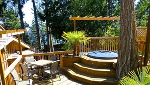 A wooden deck with a hot tub, seating area, and a view of the surrounding forest. - Handsome Dan's at Otter Point (Juan de Fuca Electoral Area)