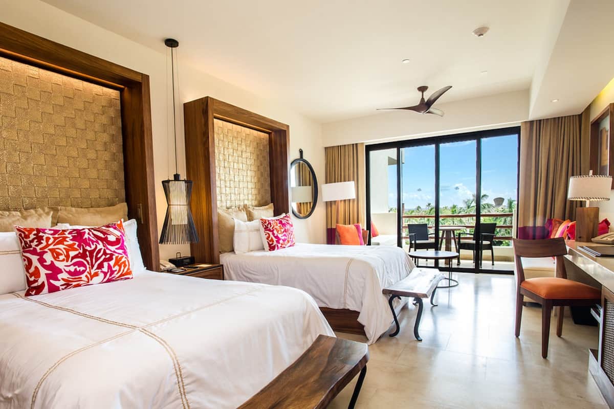 Quarto de hotel com duas camas, uma escrivaninha, uma cadeira, uma mesa de jantar e uma janela grande com vista.