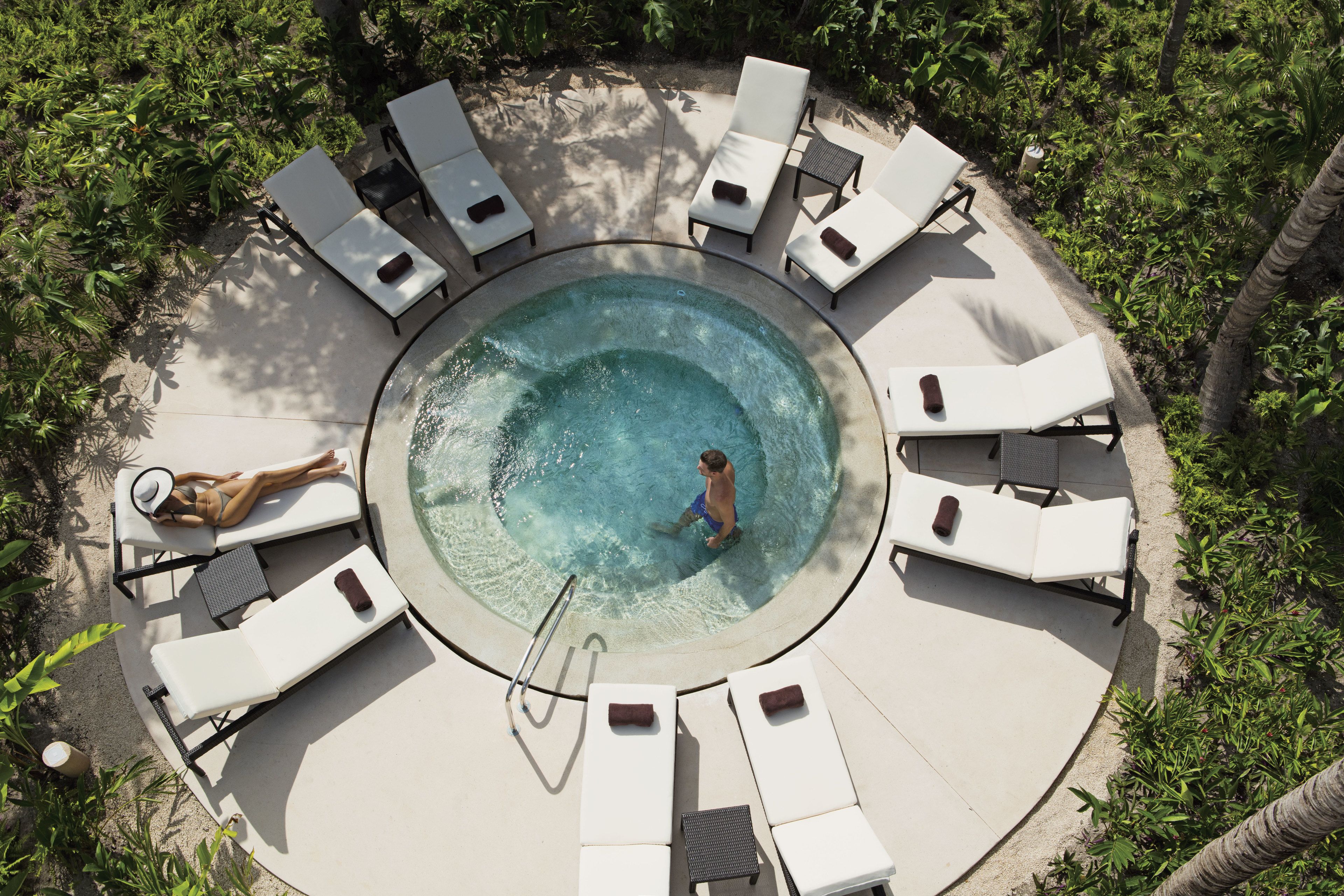 Une piscine circulaire entourée de chaises longues, un homme dans l’eau et une femme qui prend un bain de soleil.