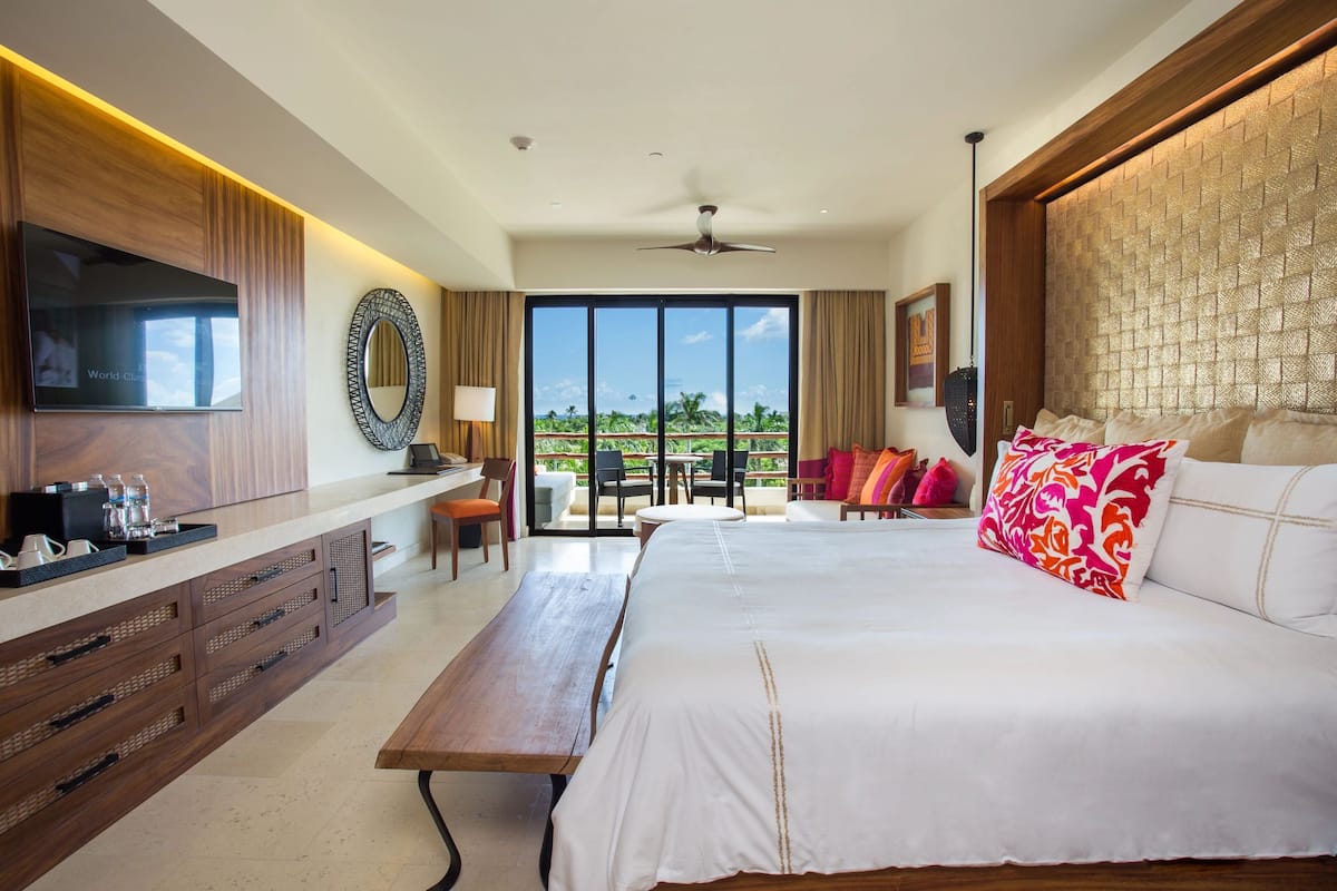 Quarto de hotel moderno com uma cama grande, televisão, escrivaninha com cadeira e varanda com vista para o exterior.