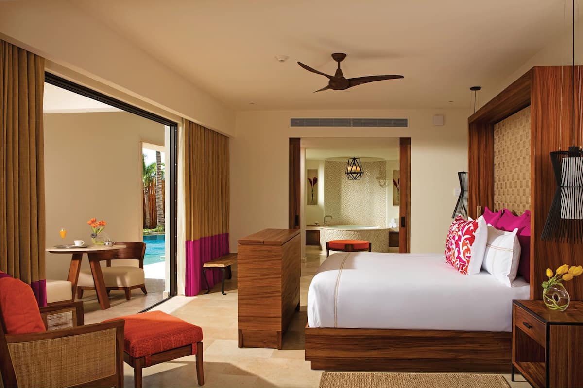 Quarto de hotel com cama, escrivaninha, cadeira, mesa pequena, banheiro e vista para o oceano.