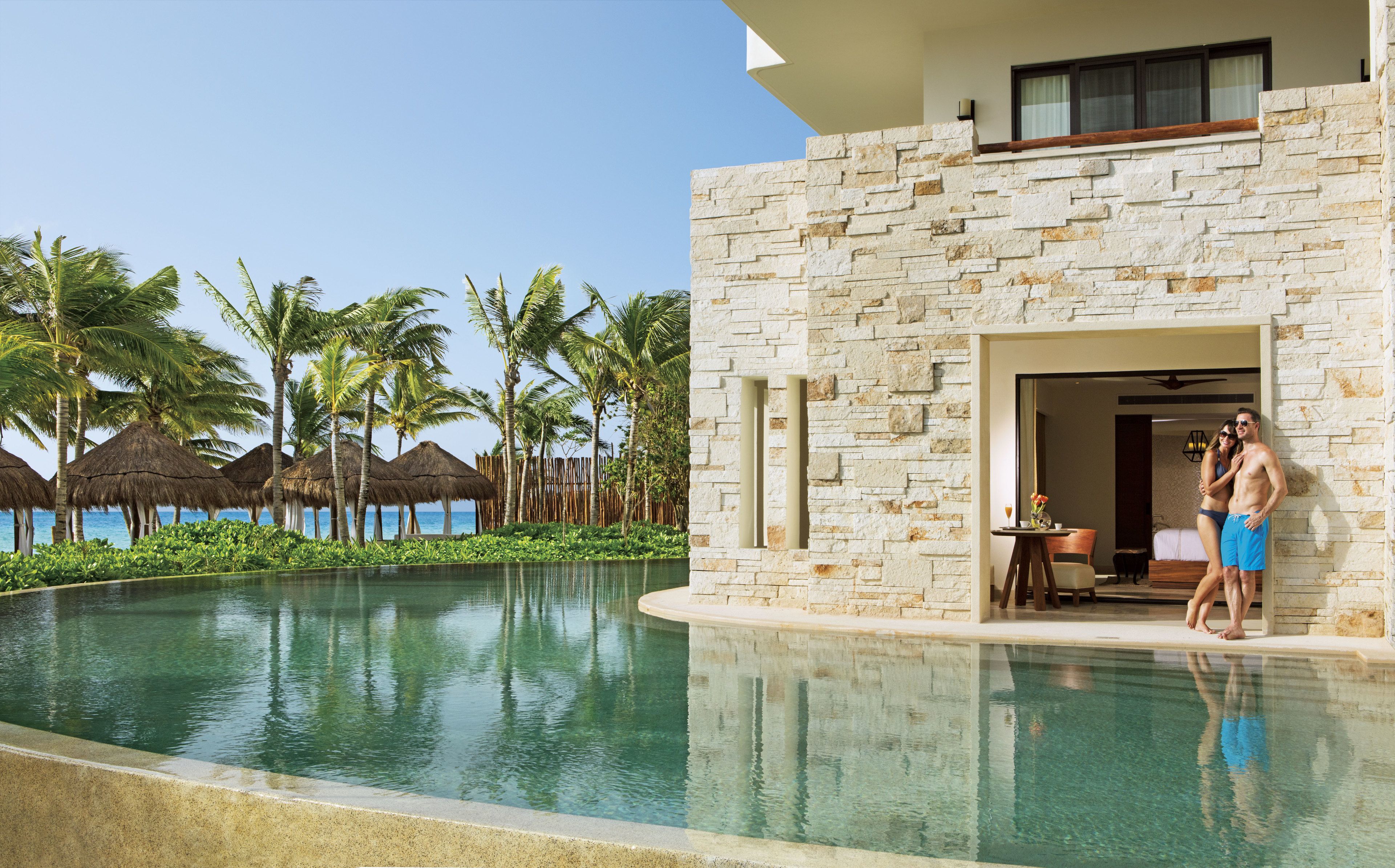 A resort with a stone exterior, a pool, and palm trees.