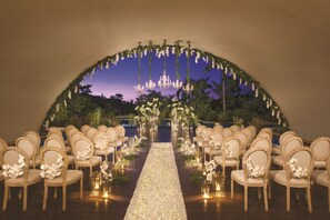 An indoor venue with a wooden floor, rows of beige chairs, and a floral aisle.