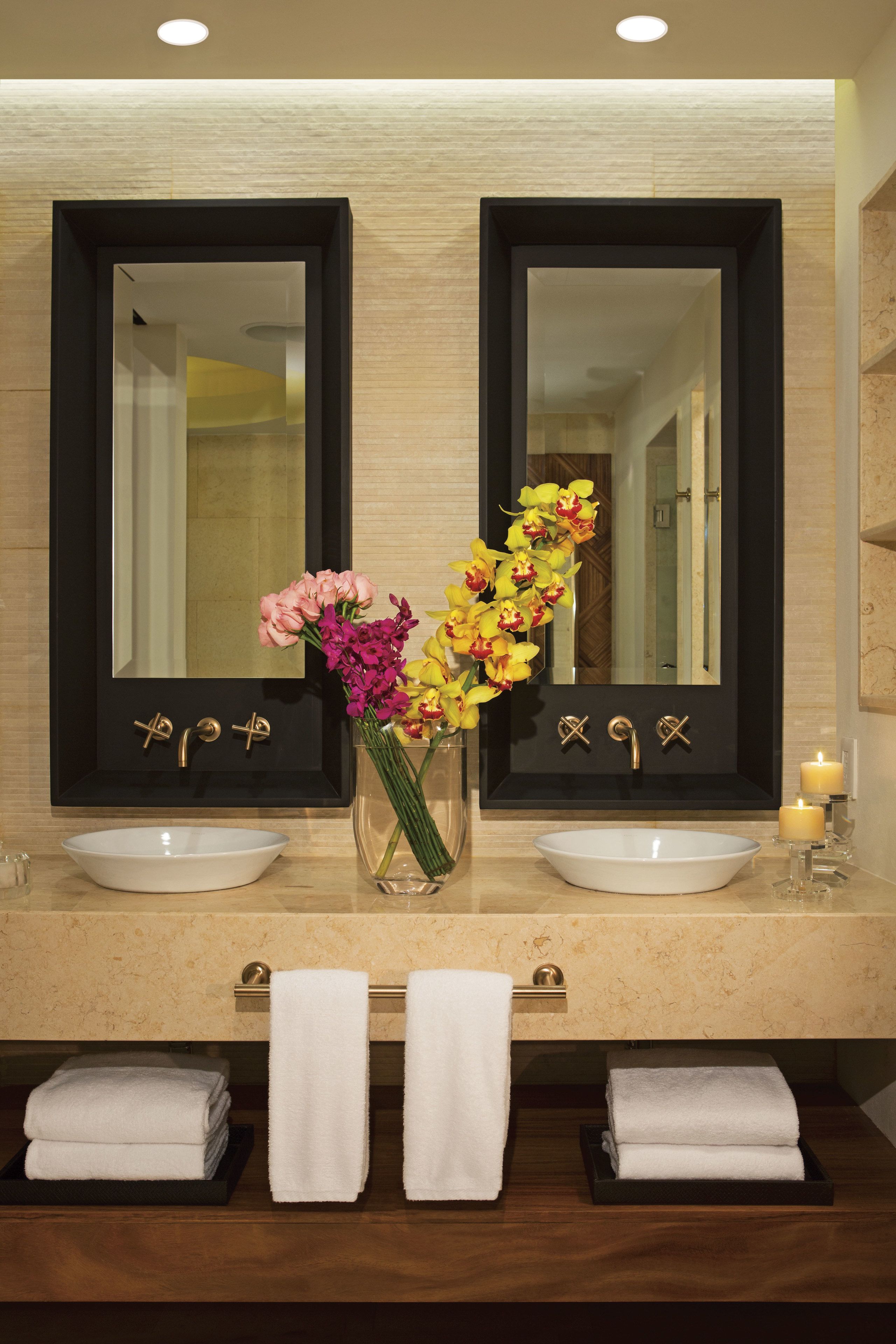 Une salle de bain avec deux lavabos, un miroir et un vase de fleurs.