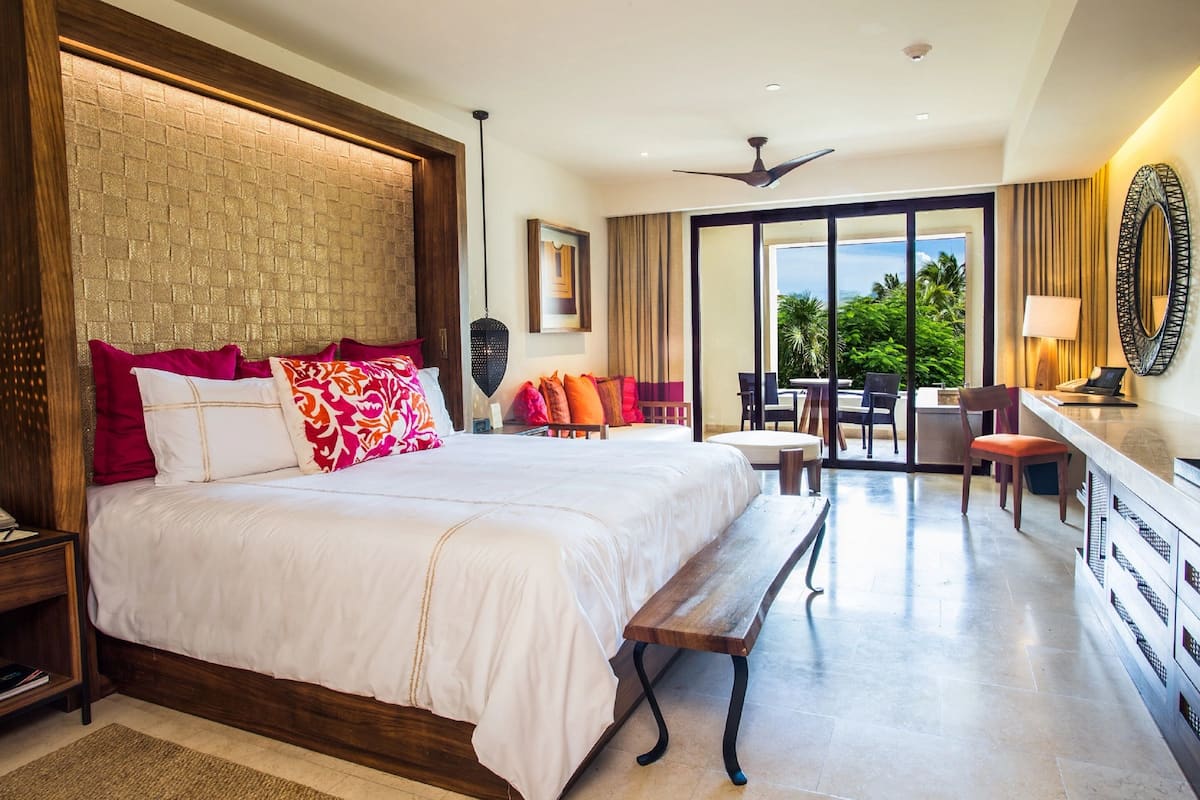 Um quarto espaçoso com uma cama grande, cabeceira de madeira, um banco e uma área de jantar com cadeiras e mesa.