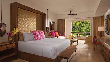 A spacious bedroom with a large bed, a wooden headboard, a bedside table with a vase of flowers, and a view of a lush garden through a large window.