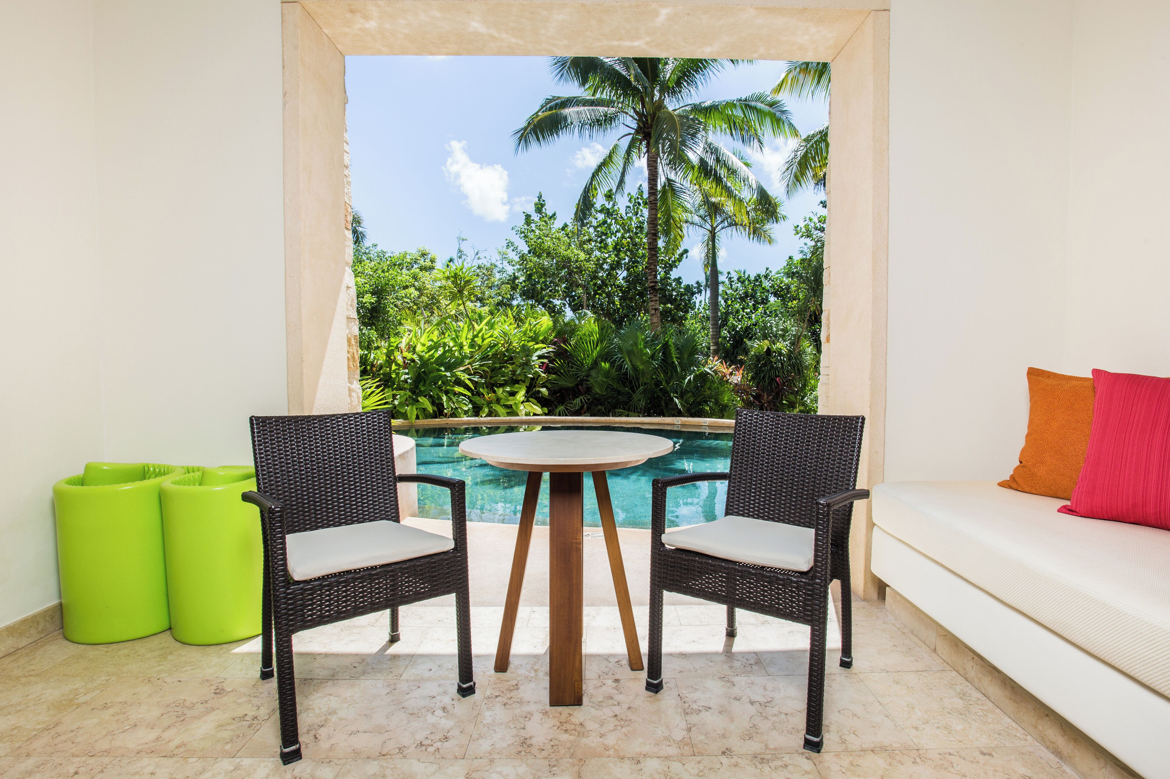 A balcony with a pool, wicker chairs, a white sofa, and a view of palm trees.