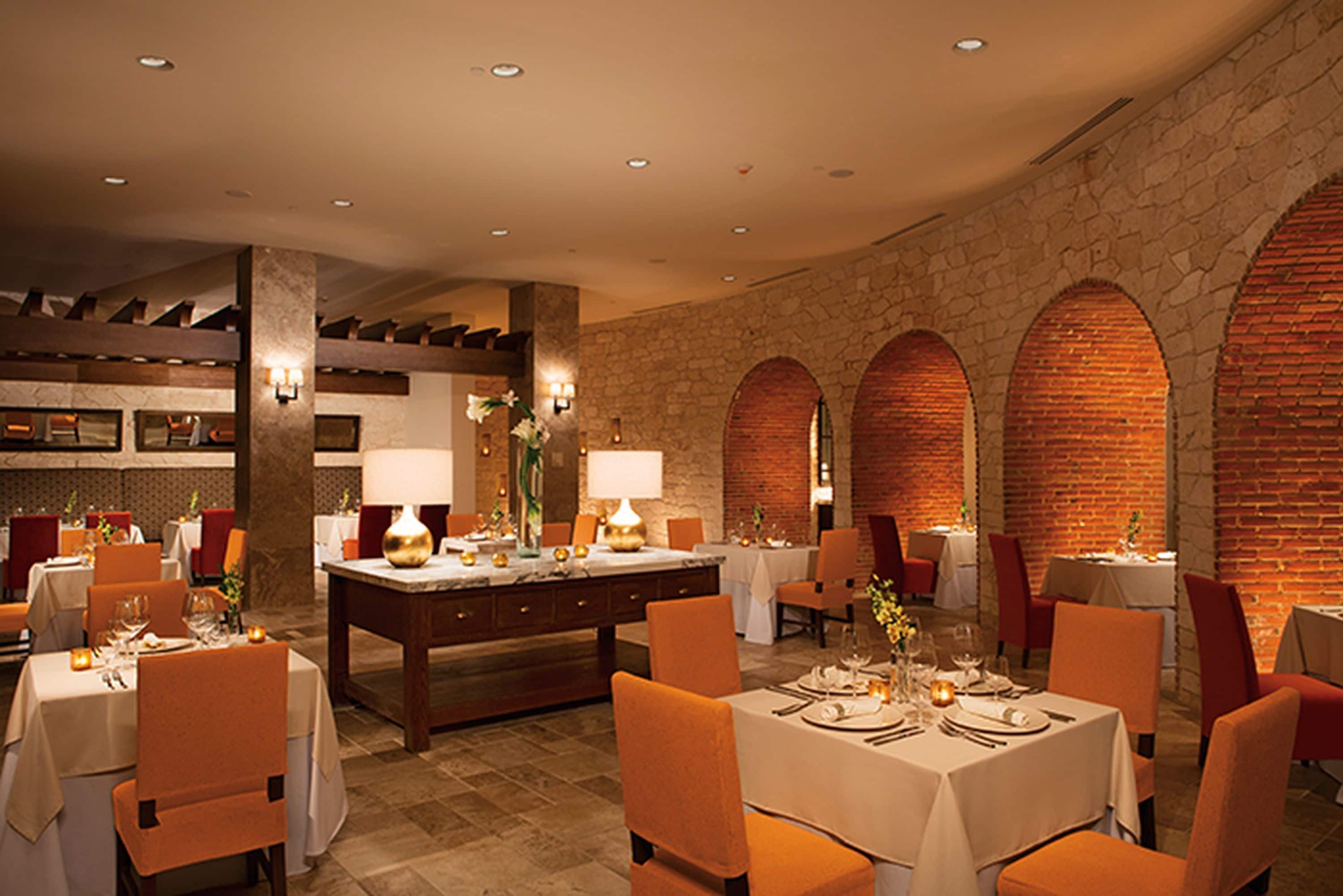 A restaurant with tables set for dining, featuring stone walls and arched brick structures.