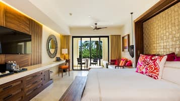 A hotel room with a large bed, a desk with a TV, a balcony with chairs, and a ceiling fan.