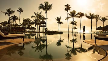 Un área de piscina tranquila con palmeras y sillones de descanso, que refleja el paisaje circundante.