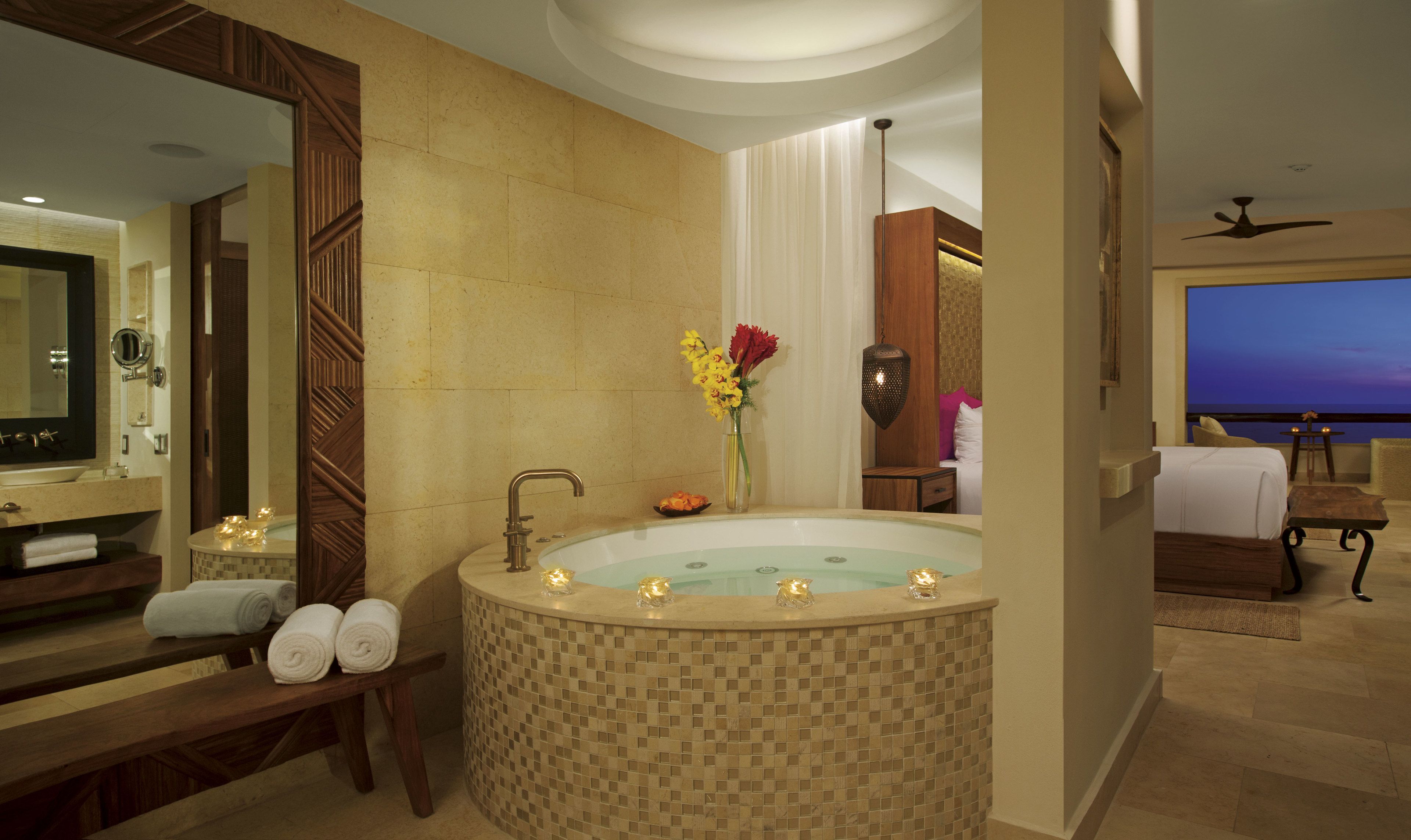 A modern bathroom with a large bathtub, a vanity with a mirror, and a bed in the adjacent room.