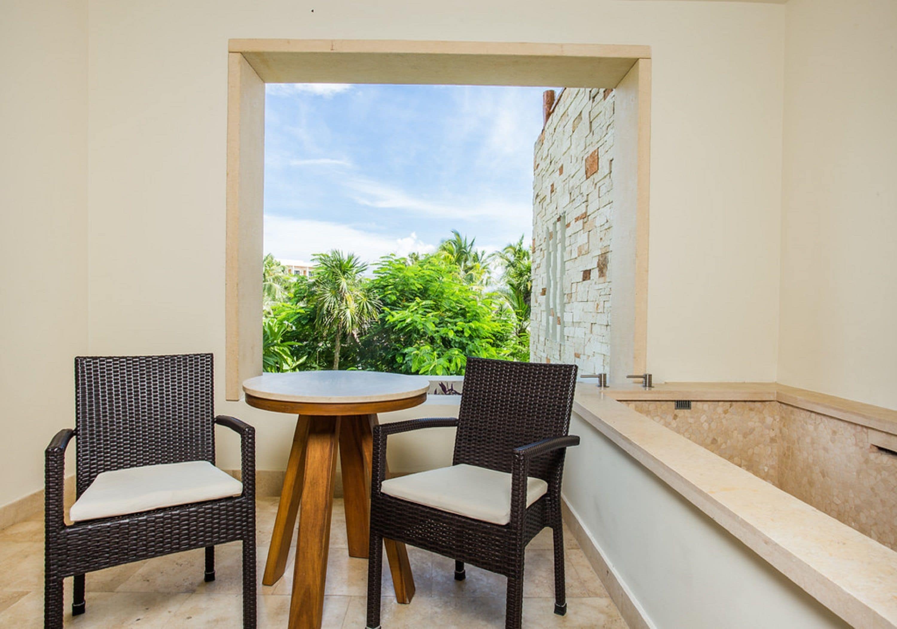 A balcony with two wicker chairs and a round wooden table.