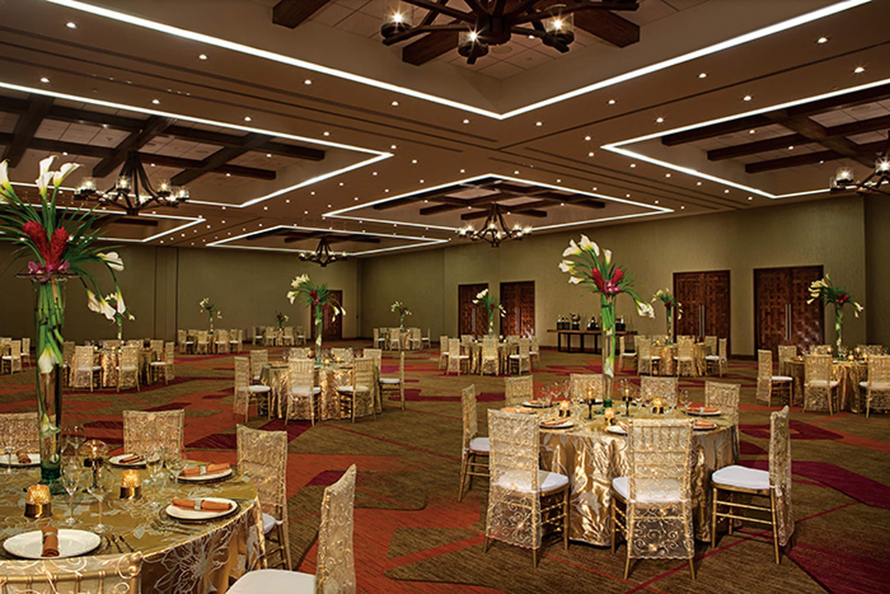 Un salón de banquetes con mesas redondas, sillas y centros de mesa florales.