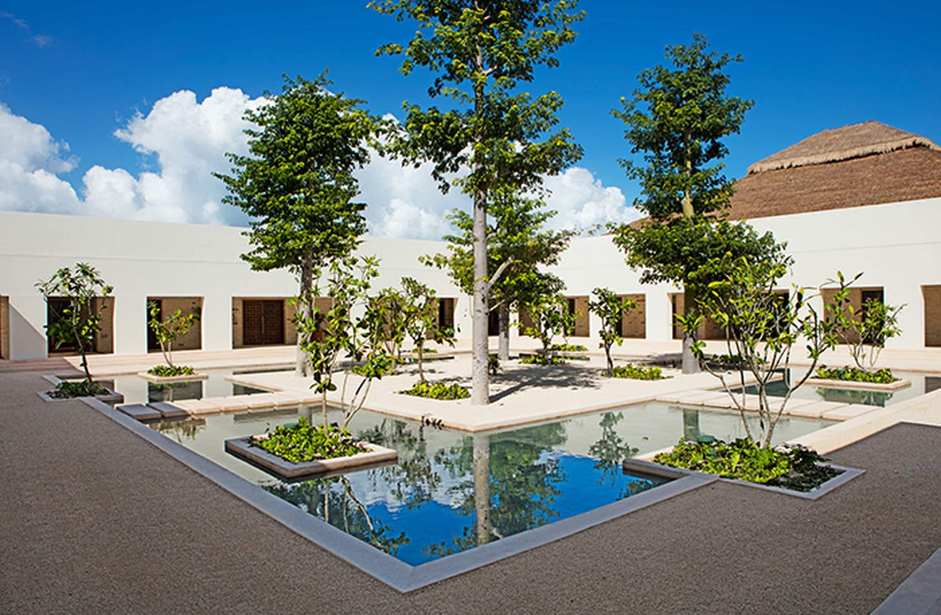 Un patio con piscina central, rodeado de árboles y edificios de techo plano.