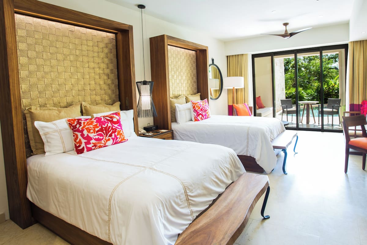 Quarto de hotel com duas camas, uma janela grande e uma varanda com área de estar externa.