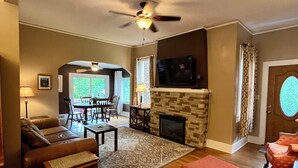 A living room with a fireplace, a ceiling fan, a television, and a dining area with a table and chairs. - Grafton Lodge (Lake Lure)