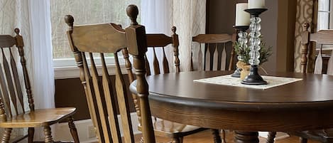 Comedor con una mesa redonda de madera, seis sillas de madera y dos velas sobre una camino de mesa.