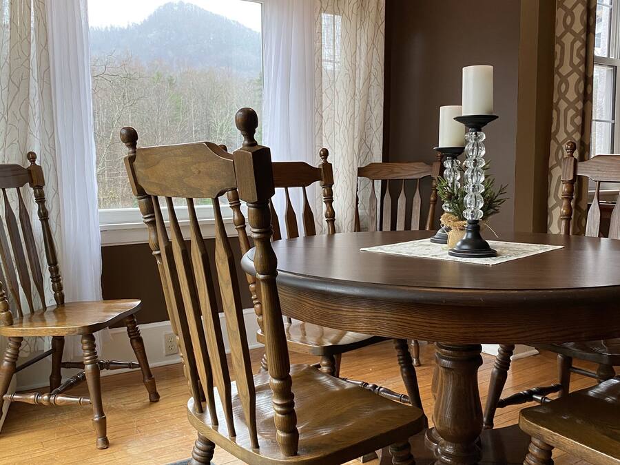 A dining room with a round wooden table, six wooden chairs, and two candles on a table runner.