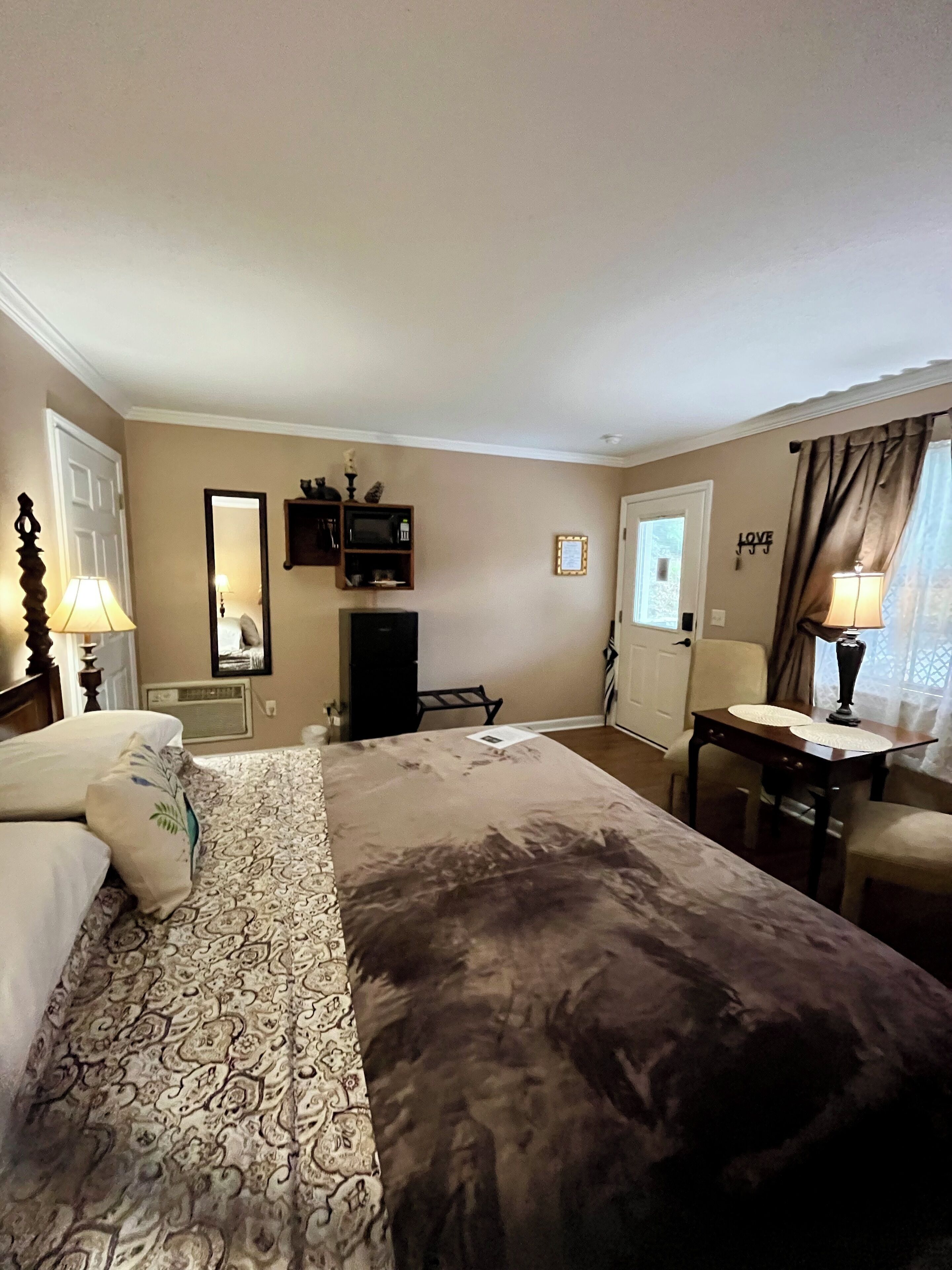 A hotel room with a large bed, a desk, a chair, a television, and a window with curtains.