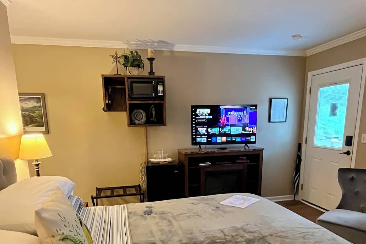 A hotel room with a bed, a television, a desk, and a door with a window.