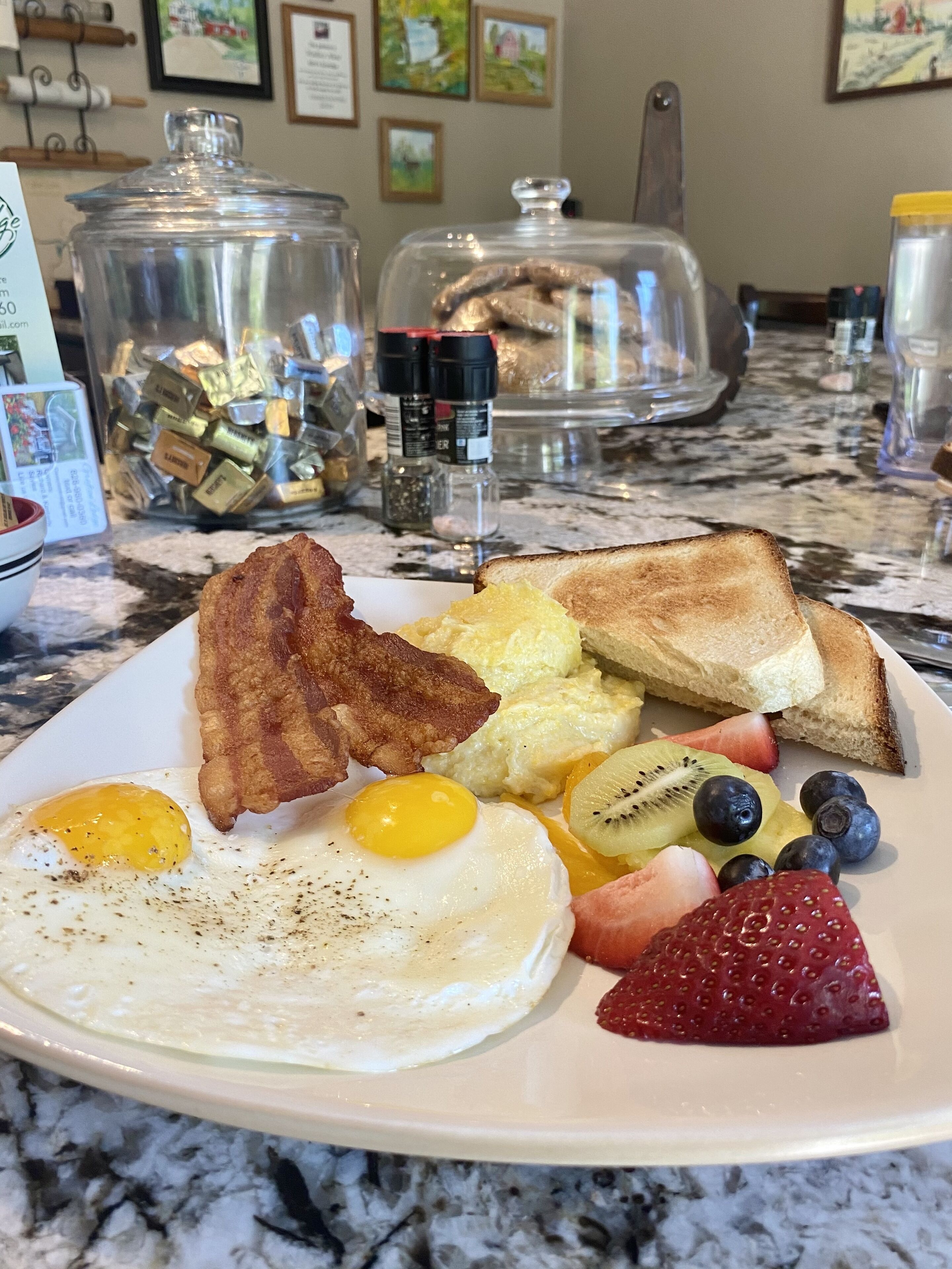 A breakfast plate with eggs, bacon, toast, fruit, and a glass container of condiments.
