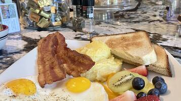 A breakfast plate with eggs, bacon, toast, fruit, and a glass container of condiments.
