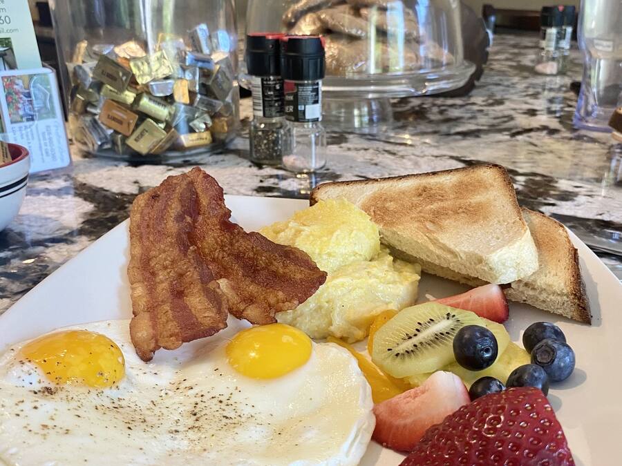 A breakfast plate with eggs, bacon, toast, fruit, and a glass container of condiments.