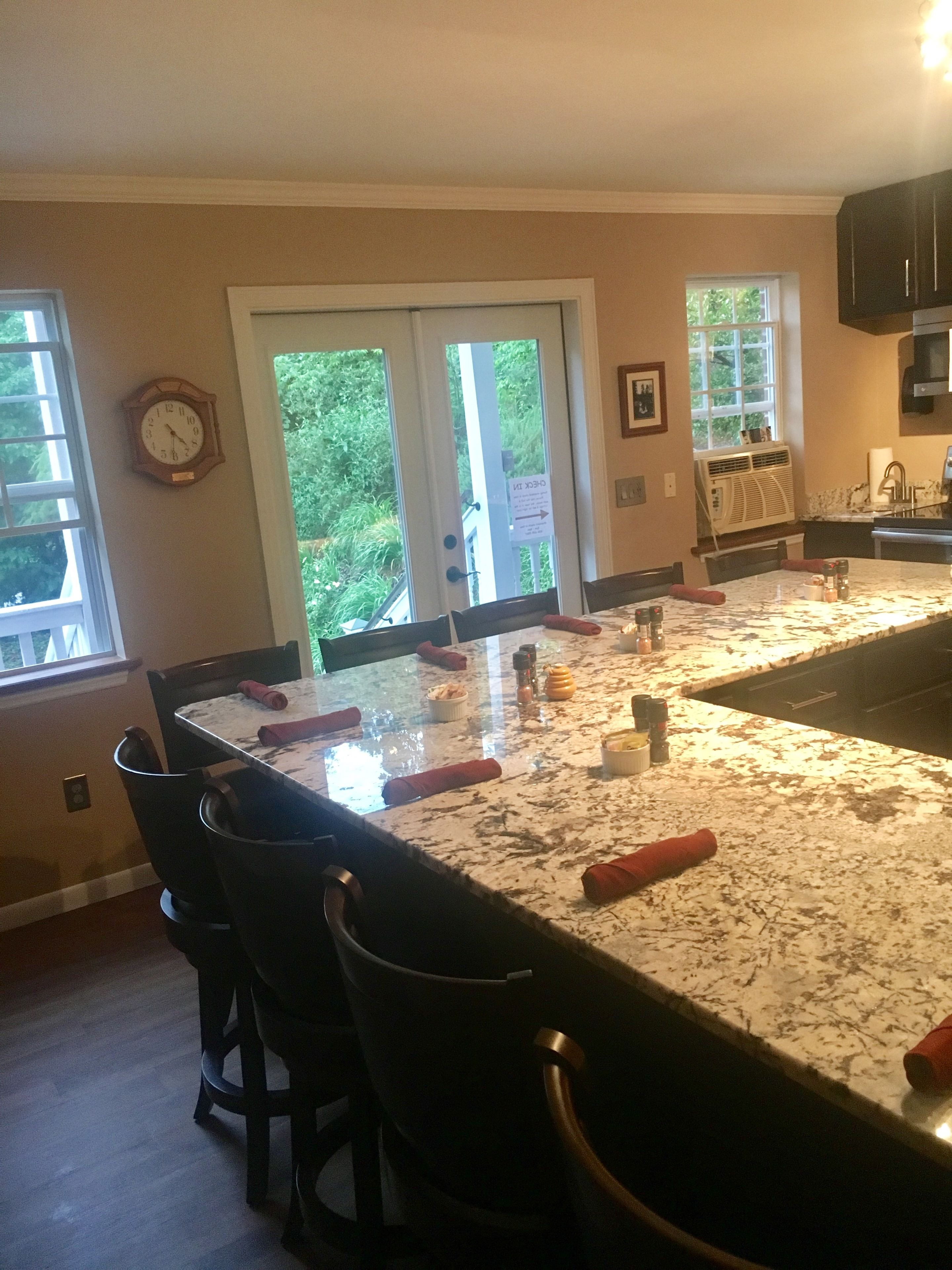 A kitchen with a large island, chairs, a clock, and a view through the glass doors.