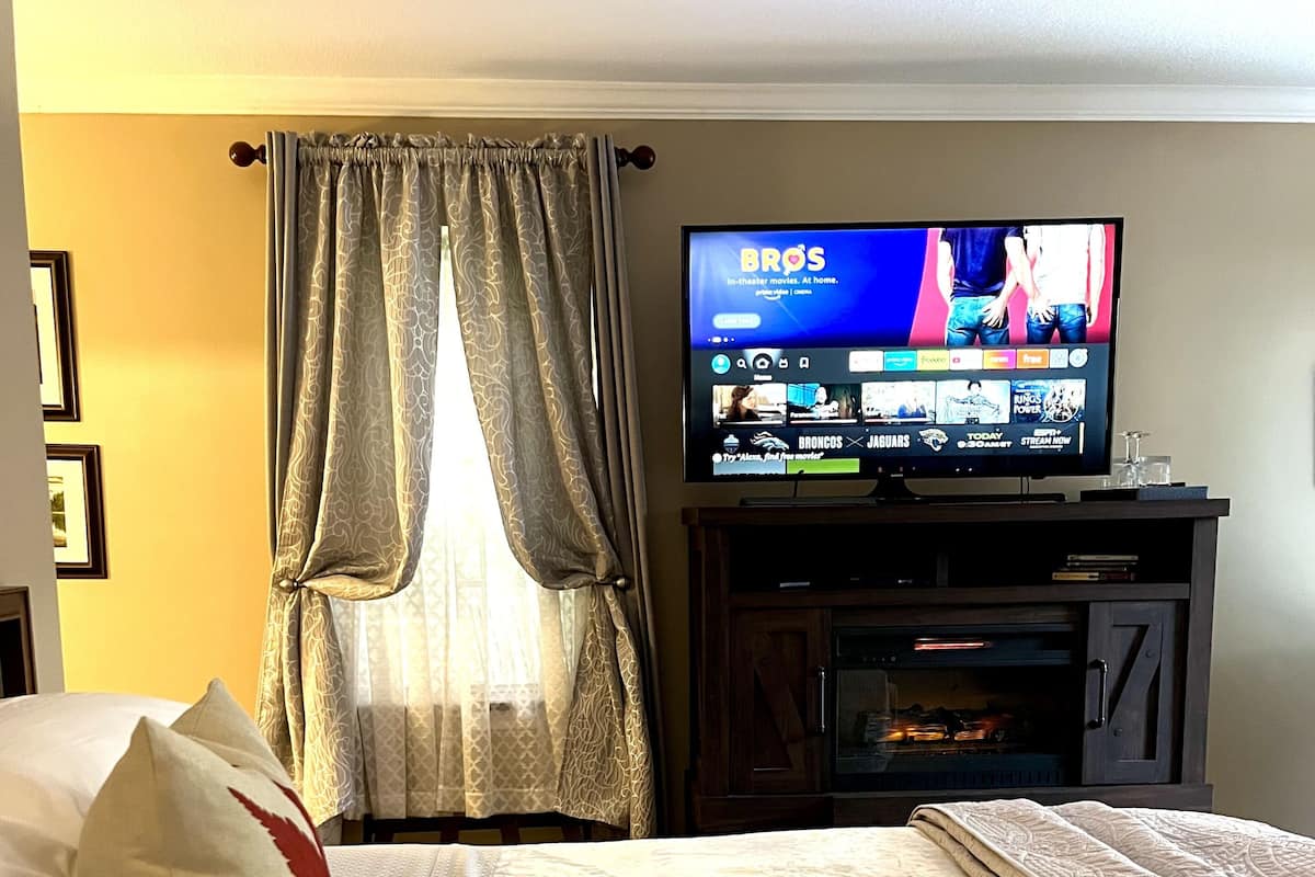A hotel room with a bed, a television displaying a movie, and a fireplace.