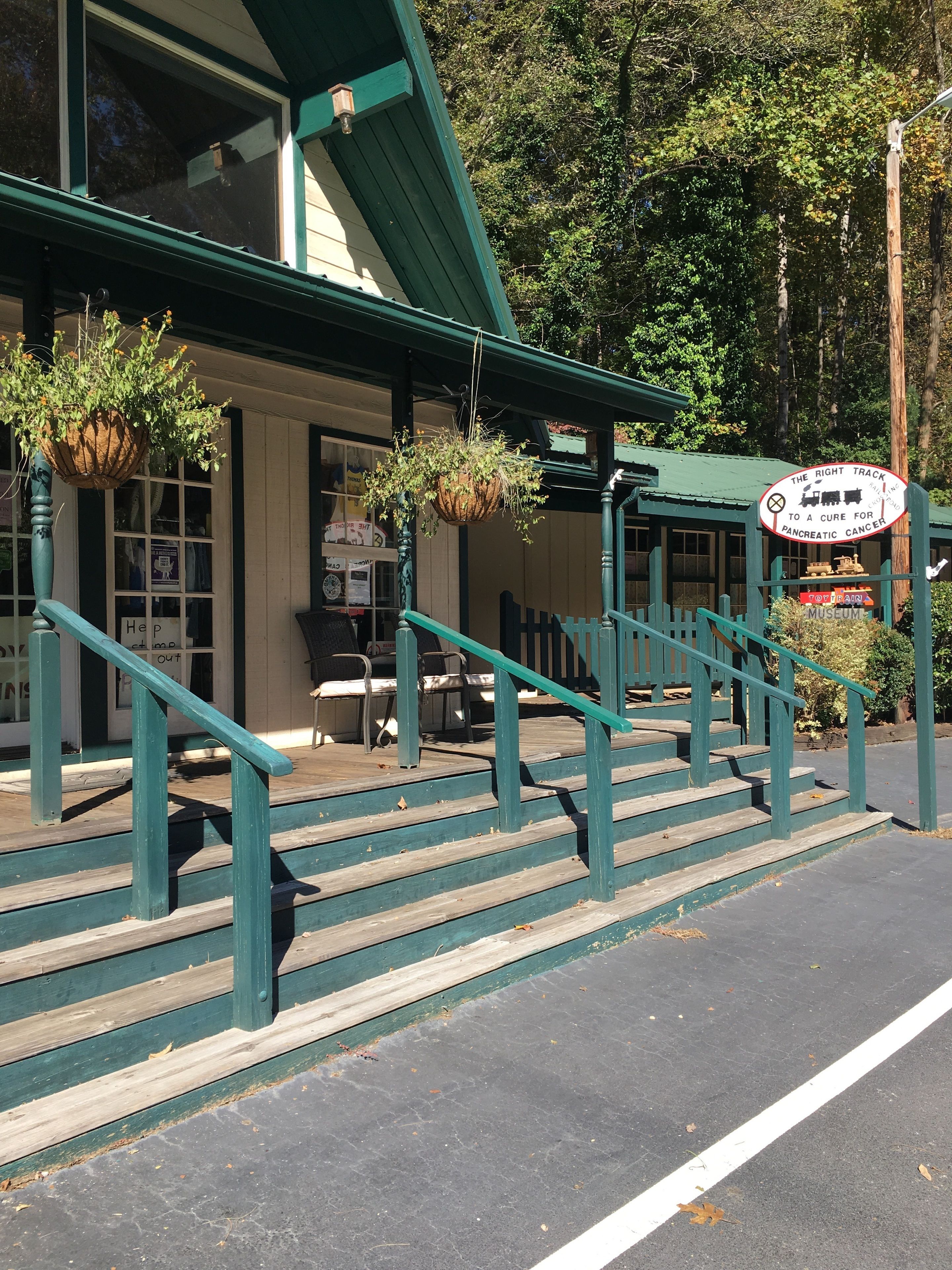 A building with a green exterior, a porch with steps, and hanging planters.