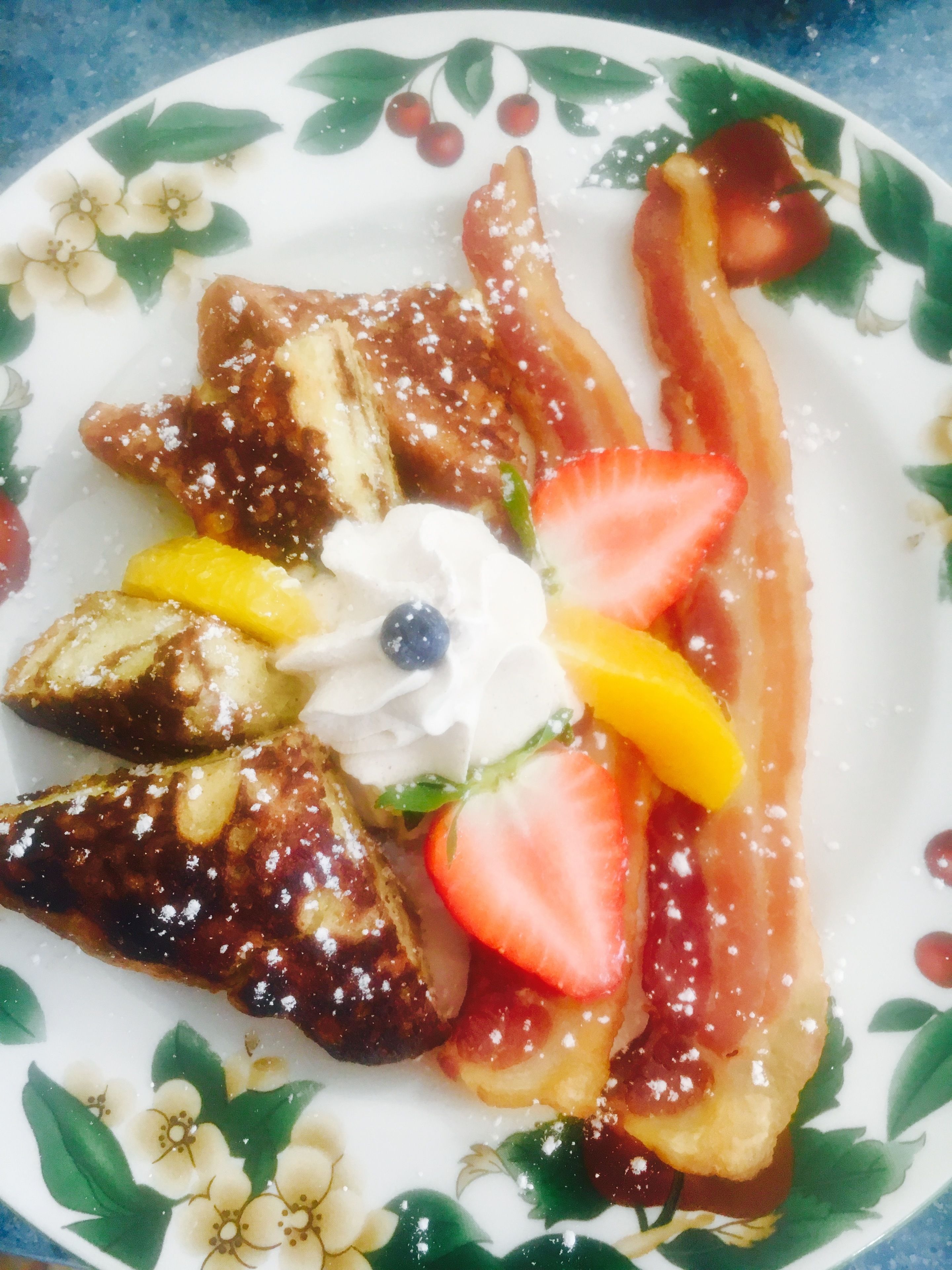 Un plato con tortitas, tocino, fresas, arándanos y crema batida.