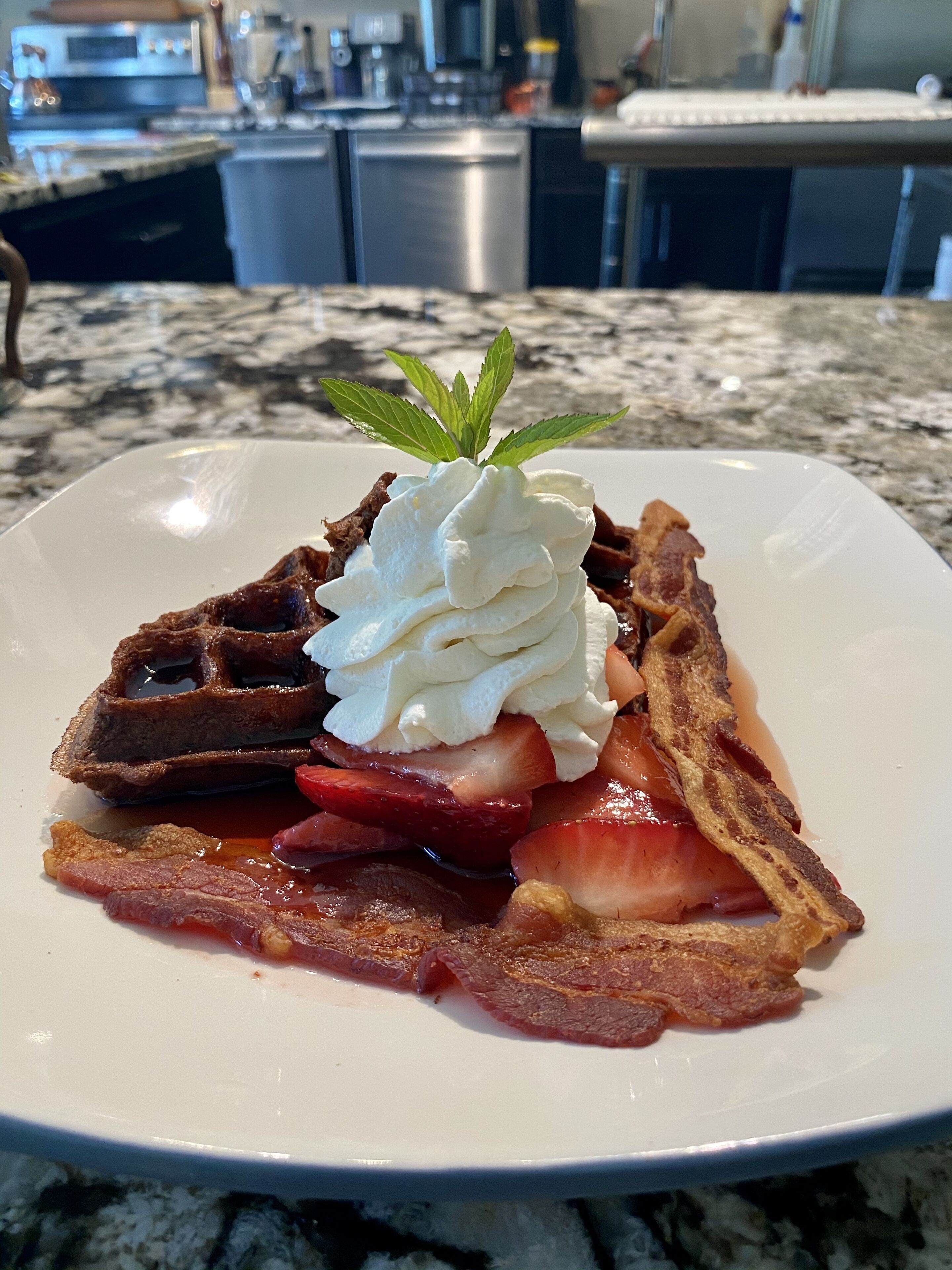 A plate of food with waffles, strawberries, whipped cream, and bacon.
