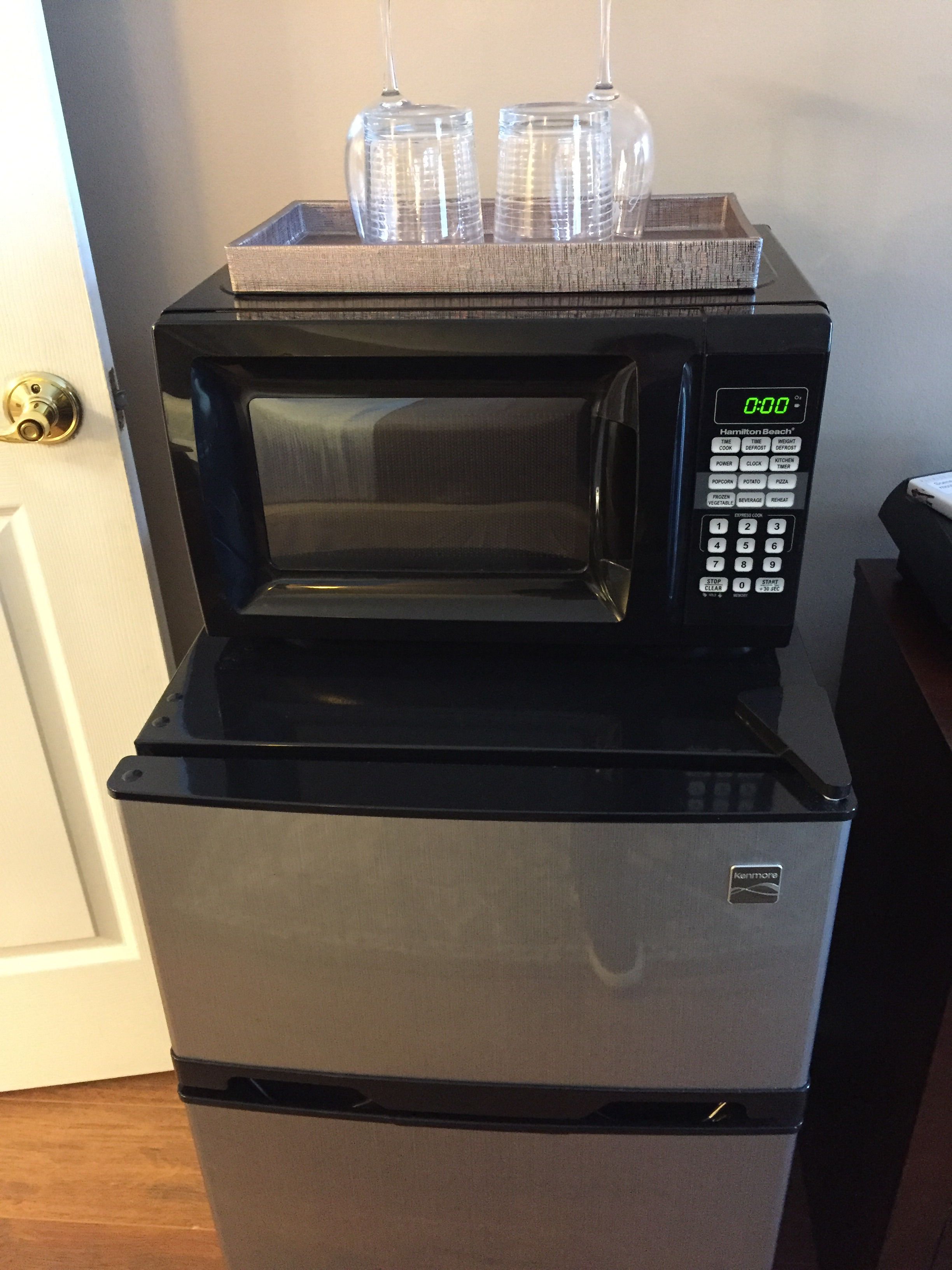 A compact kitchen setup with a microwave and refrigerator, featuring a digital display and a control panel.