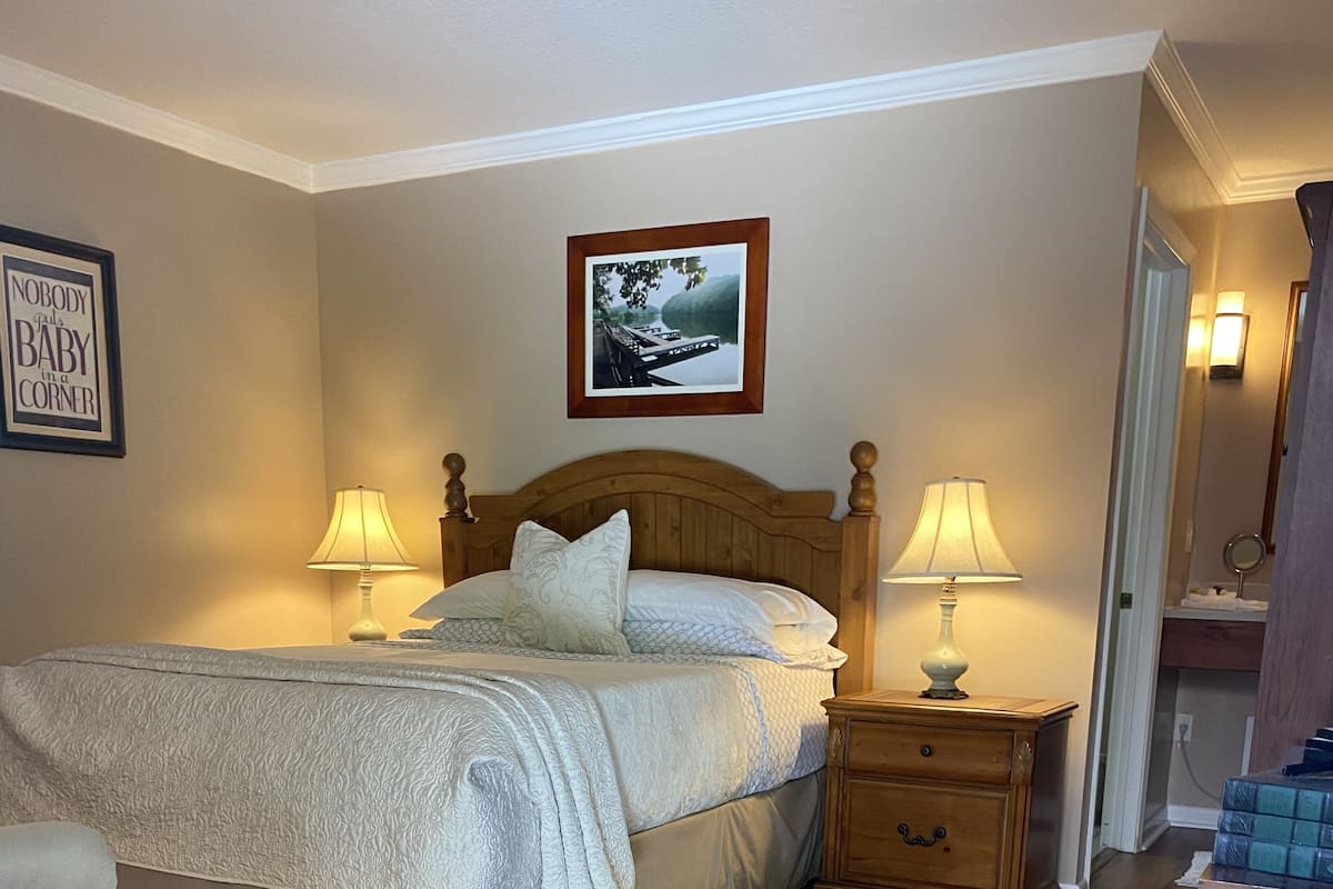 A bedroom with a wooden bed, two bedside tables with lamps, a chair, and a framed picture on the wall.