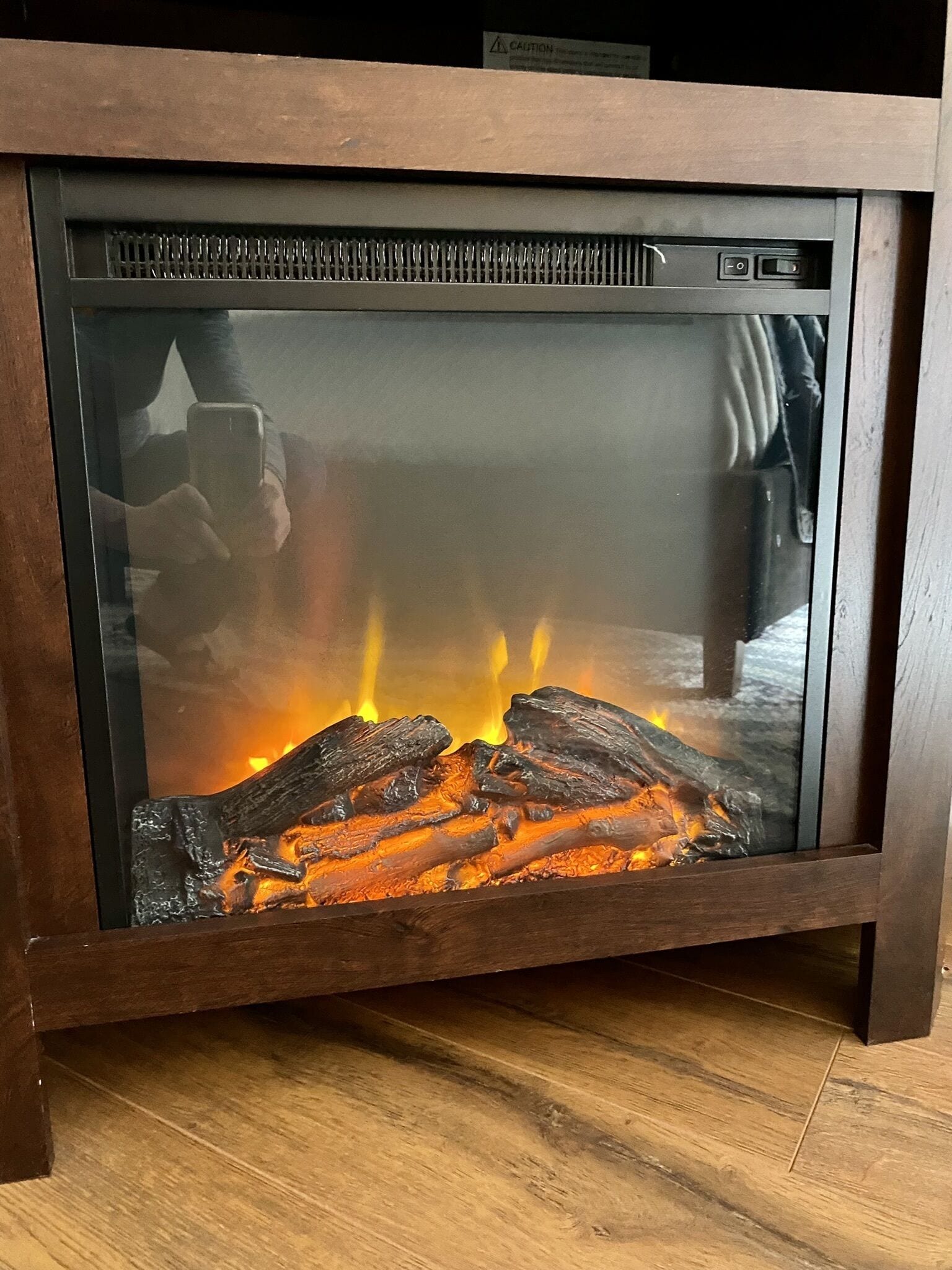 A fireplace with logs burning inside, a glass front, and a wooden frame.