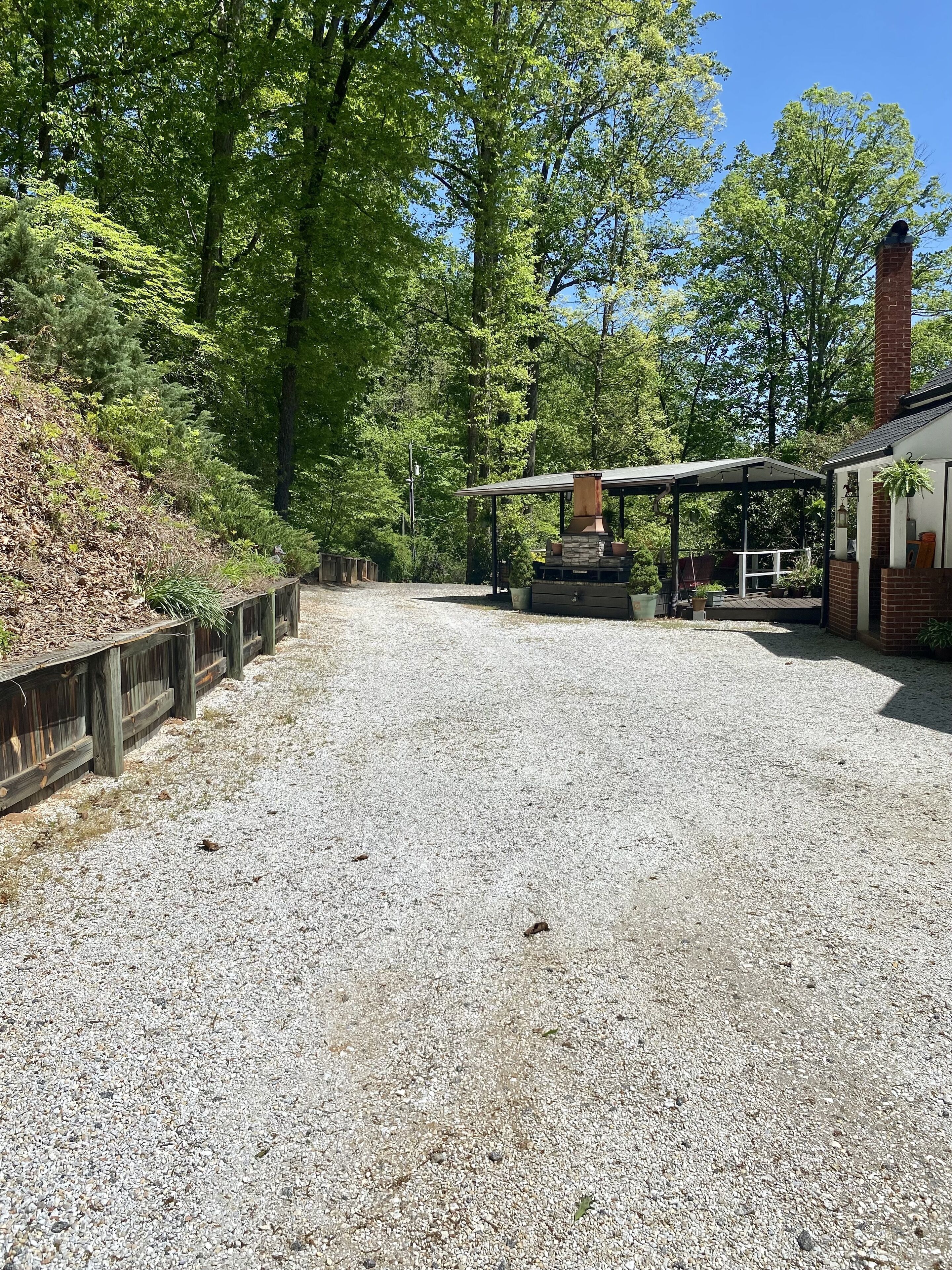 A covered outdoor area with a stone fireplace, a wooden deck, and a brick building.