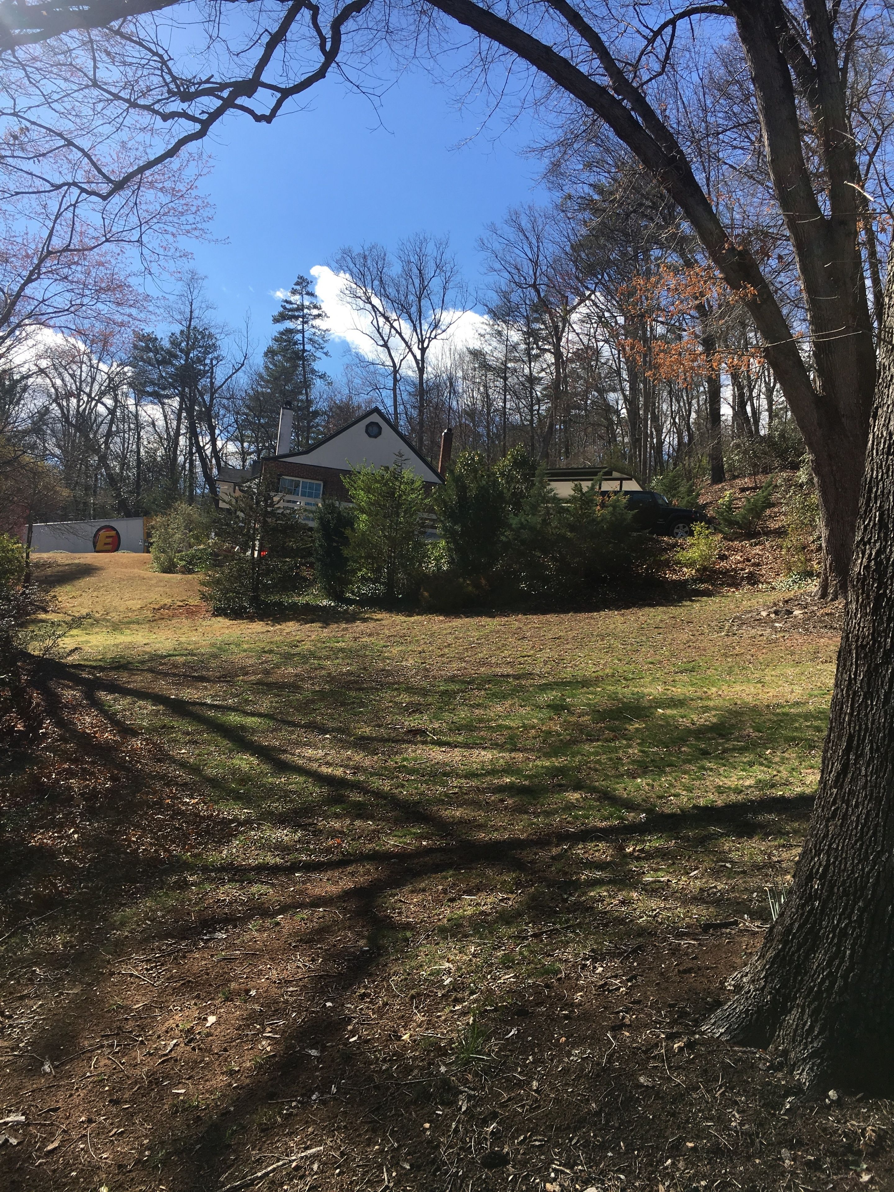 A residential area with a house surrounded by trees and a grassy yard.