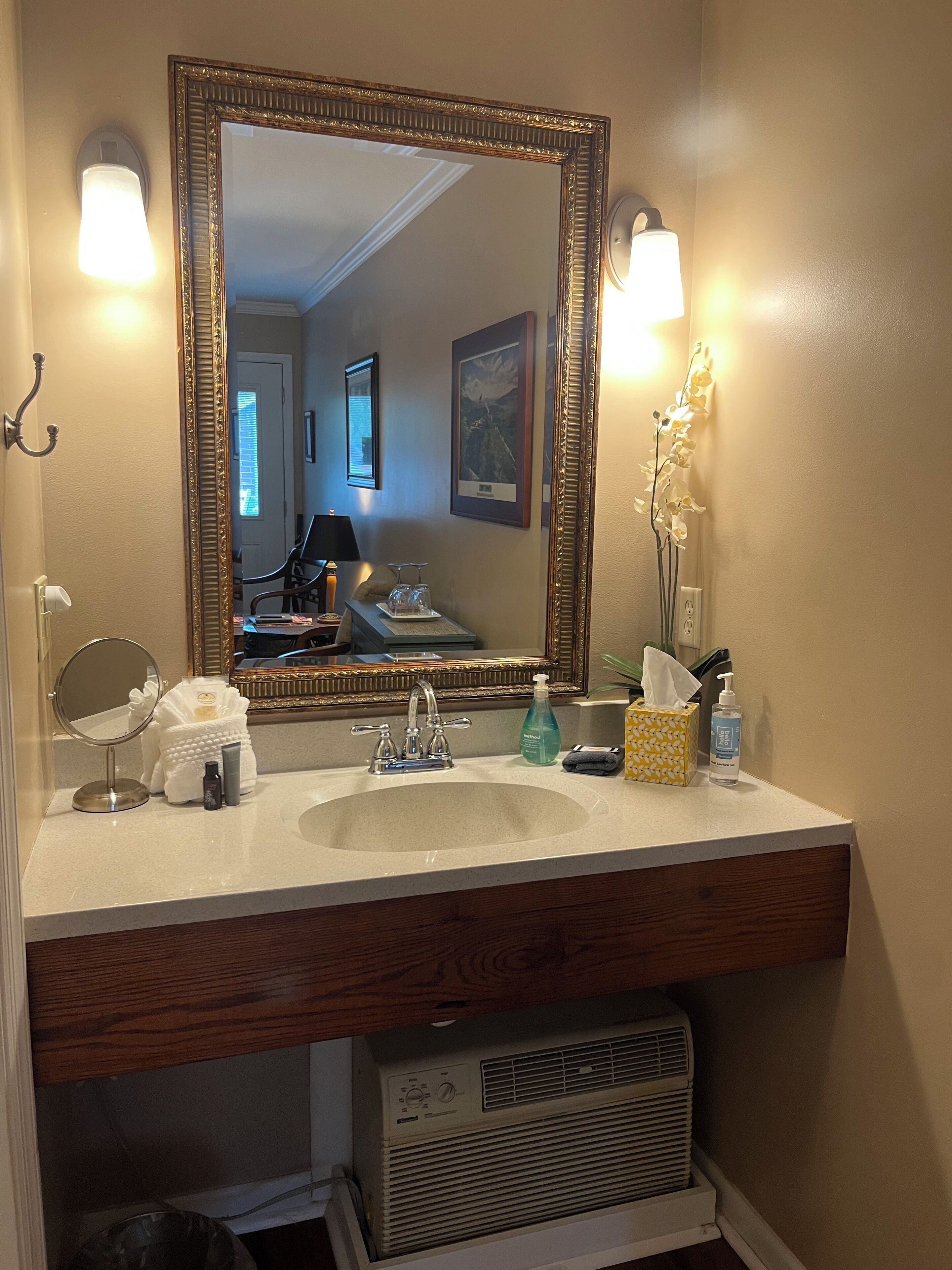 A bathroom with a large mirror, two wall-mounted lights, a sink, and a vanity.