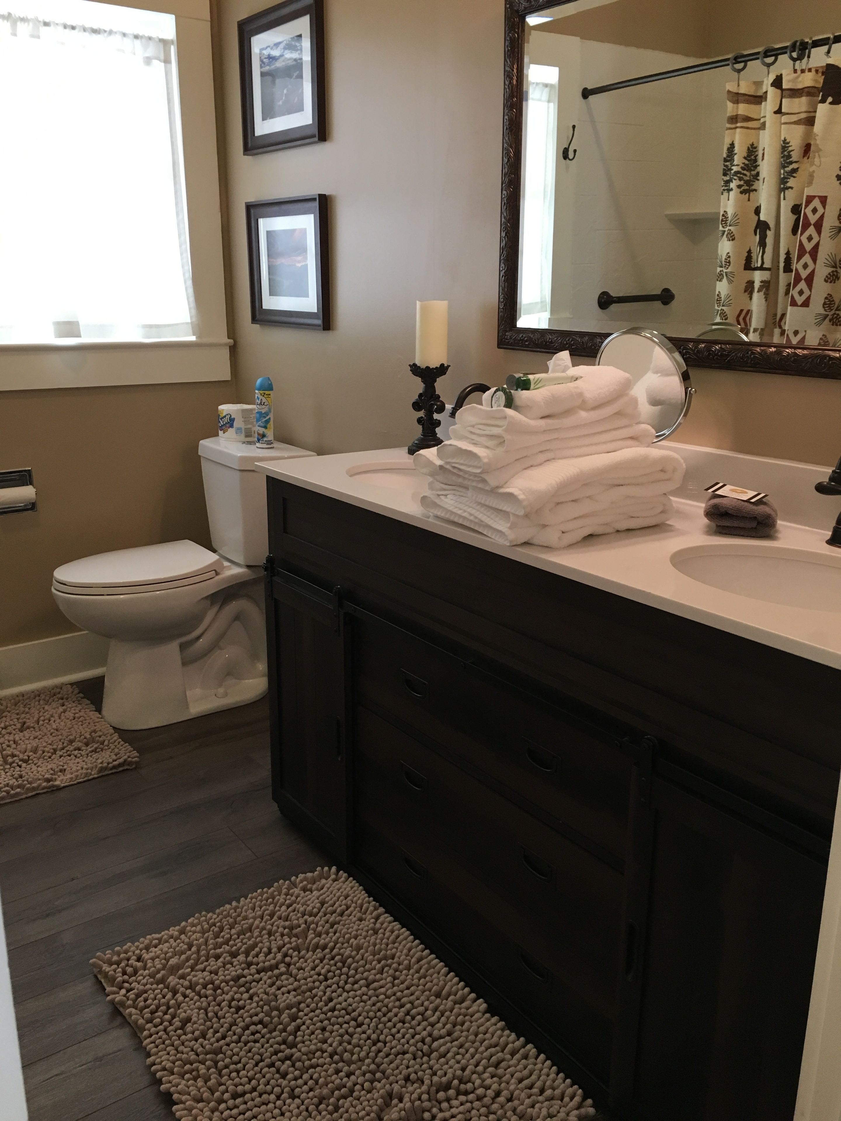 A bathroom with a toilet, sink, and mirror. There are towels stacked on the sink and a candle on the counter.