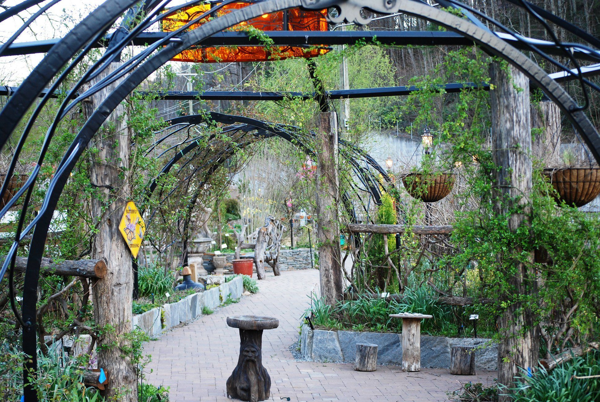 Un sentier de jardin aménagé à l’extérieur, agrémenté d’une arche en bois rustique, de jardinières en pierre et de suspensions florales.