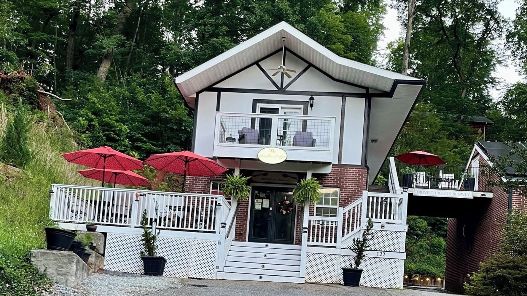 A two-story building with a balcony, red umbrellas, and a sign that reads 'Drive Through Slowly'.