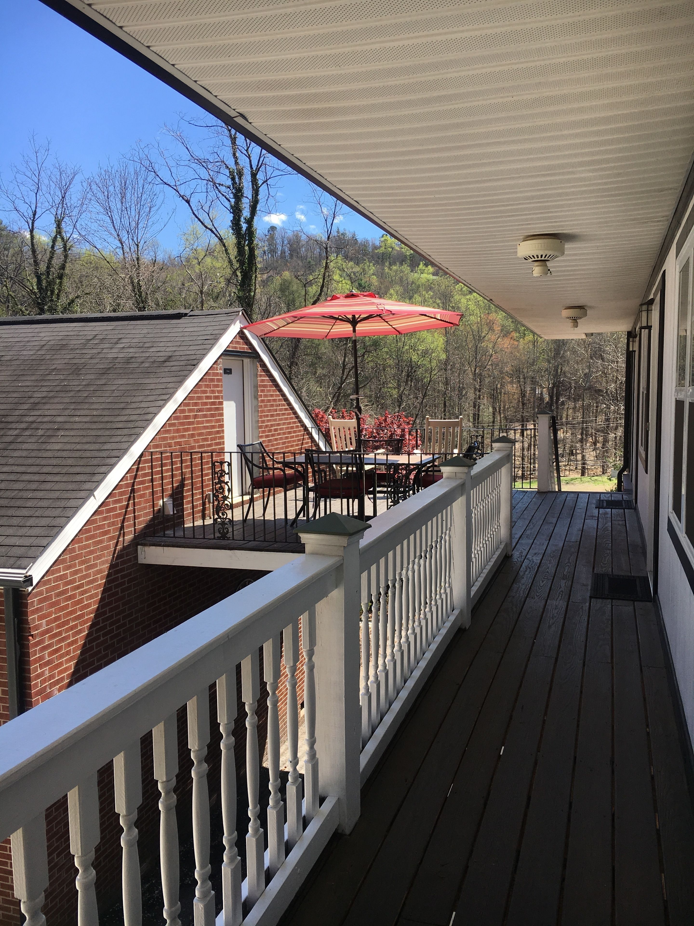 A covered porch with a brick building, outdoor furniture, and a red umbrella.