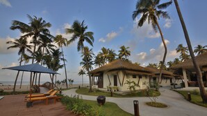 A resort with thatched-roof huts, palm trees, and a wooden deck with lounge chairs. - Eskala Hotels & Resorts Ngwe Saung (Ngwe Saung)