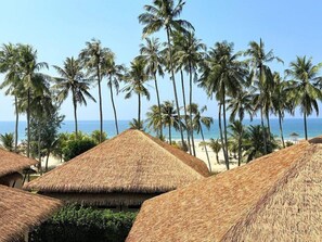 Thatched-roof structures with a beach and palm trees in the background. - Eskala Hotels & Resorts Ngwe Saung (Ngwe Saung)
