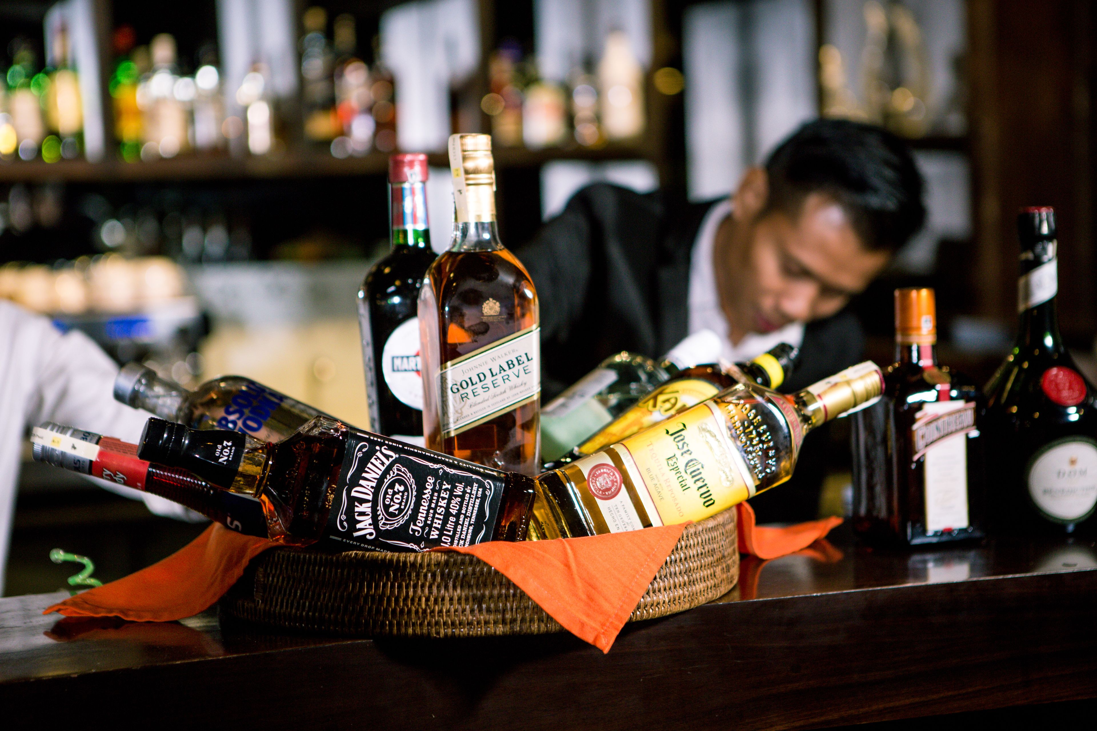 Una barra con diversas botellas de alcohol, incluyendo whisky y vino, dispuestas sobre una superficie de madera.