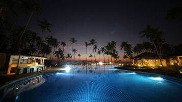 A nighttime view of a swimming pool with palm trees and a bar area.