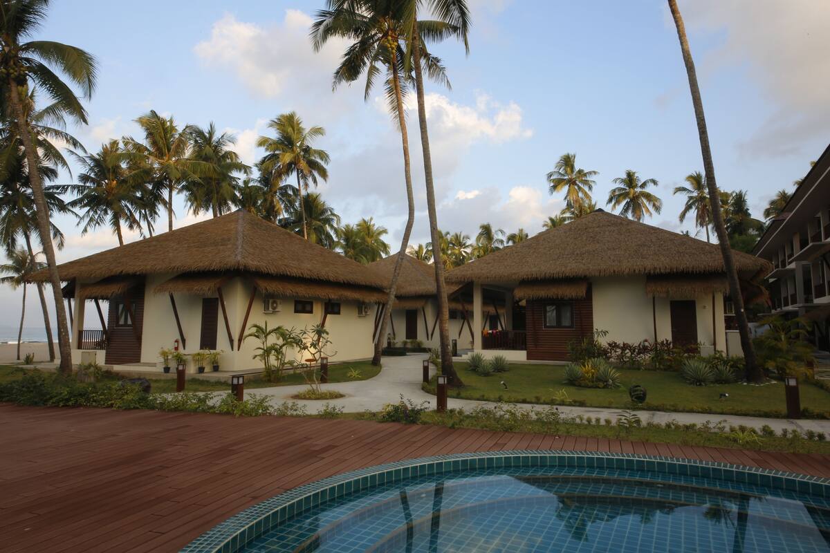 Un complexe hôtelier doté de bungalows aux toits de chaume, d’une piscine et de palmiers.