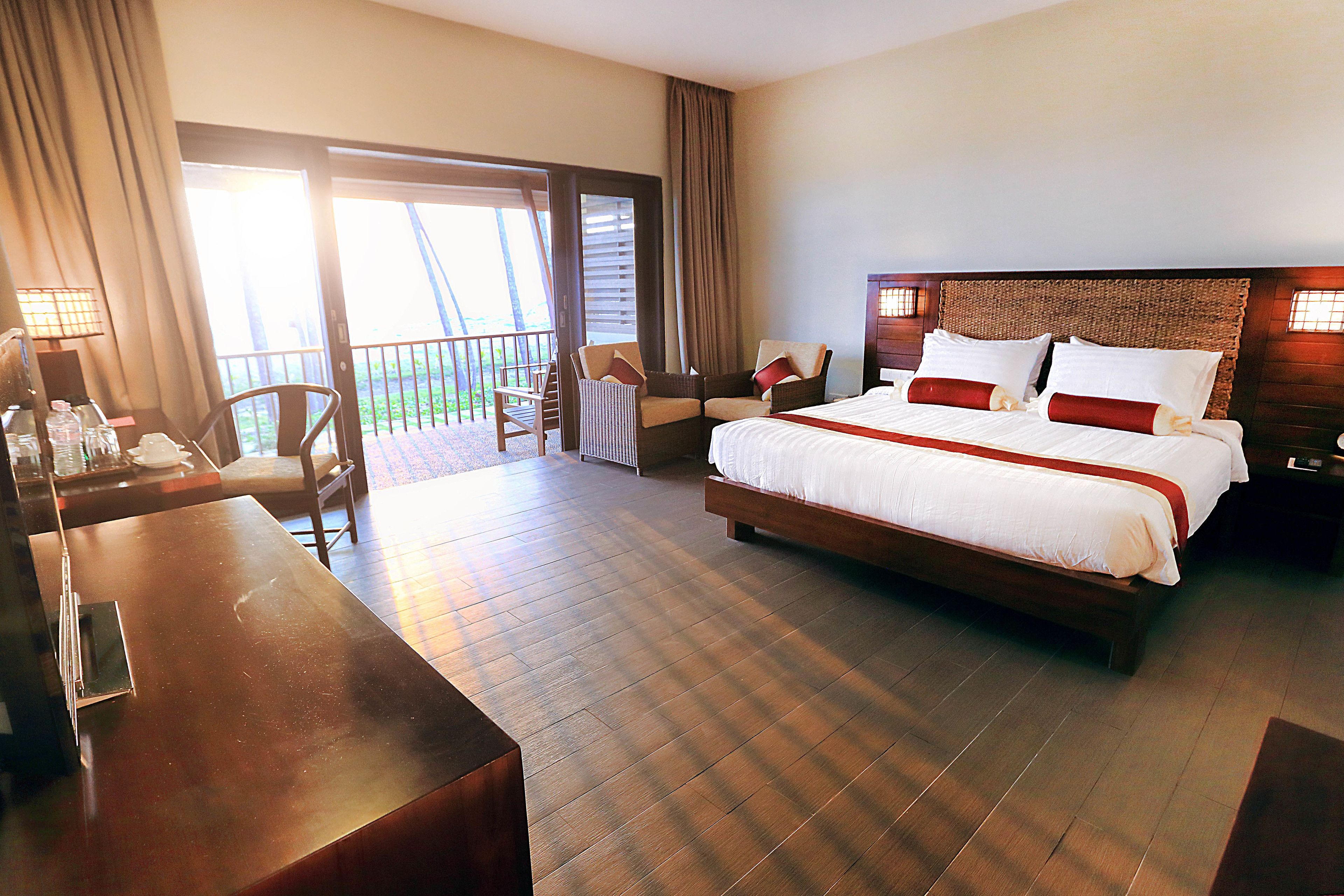 A hotel room with a large bed, a desk, and a balcony with chairs.