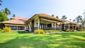 A resort with thatched-roof buildings, a well-maintained lawn, and palm trees in the background. - Eskala Hotels & Resorts Ngwe Saung (Ngwe Saung)
