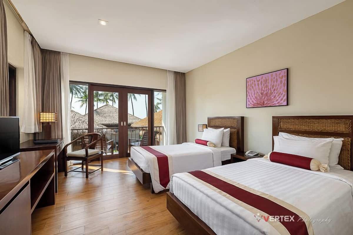 Une chambre d’hôtel avec deux lits, un bureau, une chaise et un balcon donnant sur des palmiers.
